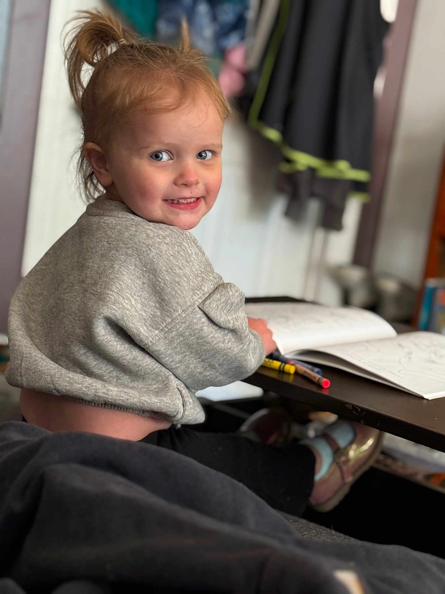 Haisley joined the competition — help win amazing prizes! toddler, child, smiling, pony_tail, gray_sweater, coloring_book, crayons, table, shoes, socks, indoor, home, furniture, person, portrait, happy, playful, young_child, cozy, casual