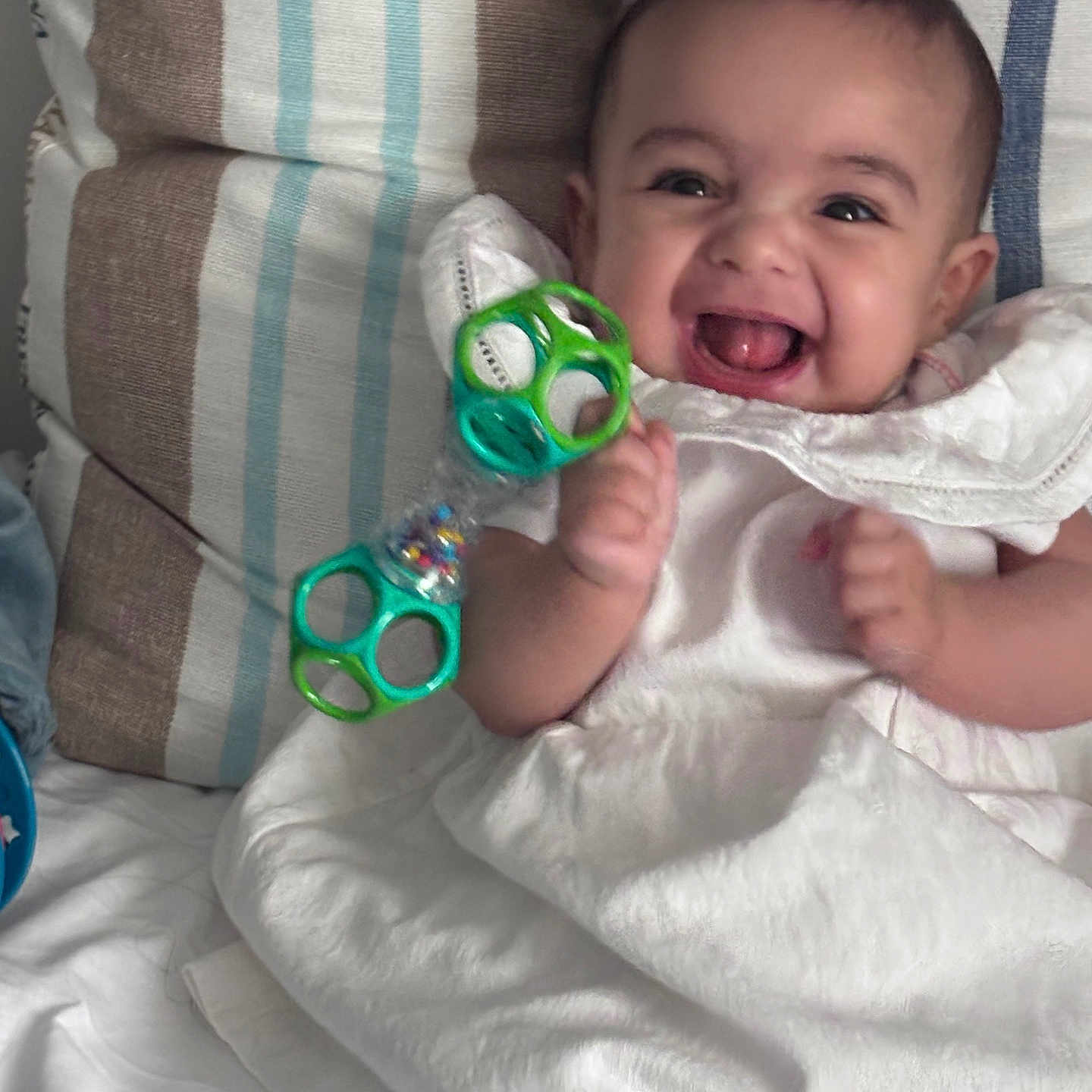 Ellia Sandia participe au concours pour gagner de l'argent avec cette photo : baby, cheerful, child, cushion, cute, fabric, face, happy, holding, indoors, infant, joyful, person, playful, sitting, smiling, striped, toy, white_dress, young