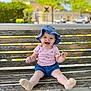 Lucia is registered to the contest to win money with this photo: baby, child, smiling, sitting, bench, wood, outdoor, hat, blue_hat, pink_shirt, shorts, happy, cute, sunny_day, feet, socks, person, nature, greenery, daytime