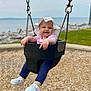 baby, child, swing, playground, hat, white_shoes, leggings, grass, water, rocks, wood_chips, outdoor, happy, smiling, person, seat, summer, daylight, nature, fun