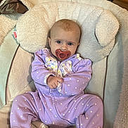 Octavia is registered to the contest to win money with this photo: baby, infant, pacifier, purple_onesie, polka_dots, plush_chair, soft_toys, indoor, wood_floor, cute, child, face, sitting, clothing, baby_seat, comfort, infant_wear, expression, head_support, footed_pajamas
