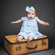 Eliza joined the competition — help win amazing prizes! baby, child, blue_dress, bow, sitting, vintage_suitcase, studio, portrait, cute, infant, smiling, barefoot, expression, isolated, gray_background, person, young_child, studio_lighting, fashion, accessory