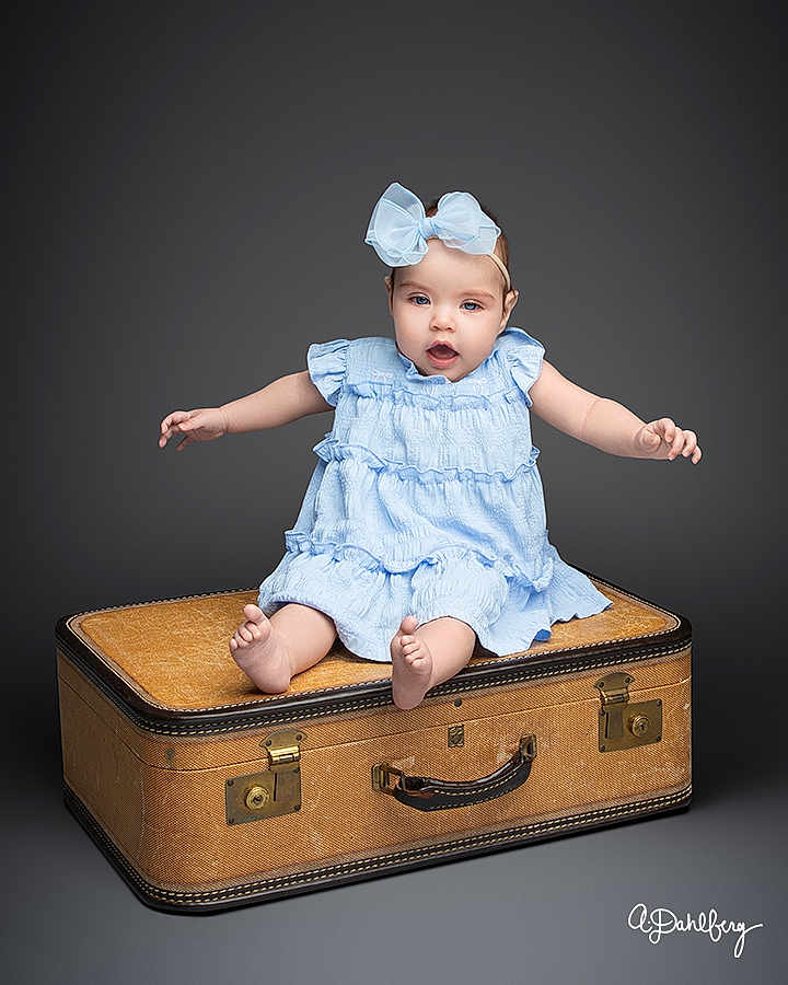 Eliza joined the competition — help win amazing prizes! baby, child, blue_dress, bow, sitting, vintage_suitcase, studio, portrait, cute, infant, smiling, barefoot, expression, isolated, gray_background, person, young_child, studio_lighting, fashion, accessory