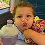 child, pout, plush_toy, purple_sippy_cup, flower_hair_clip, train_seat, window, table, cute, toddler, holding, indoor, portrait, happy, face, hair, clothing, toy, expression, seat