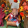 Giullian participe au concours pour gagner de l'argent avec cette photo : toddler, child, wooden_chair, blanket, pumpkin, autumn_leaves, fall_decor, flowers, plaid_fabric, green_carpet, indoor, seasonal, orange, yellow, red, casual_clothing, smiling, portrait, decorations, festive