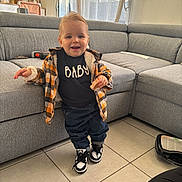 Giullian participe au concours pour gagner de l'argent avec cette photo : toddler, child, indoor, living_room, plaid_jacket, sneakers, toy, smiling, curtains, couch, floor_tiles, window, person, clothing, happy, hair, furniture, home, casual, portrait