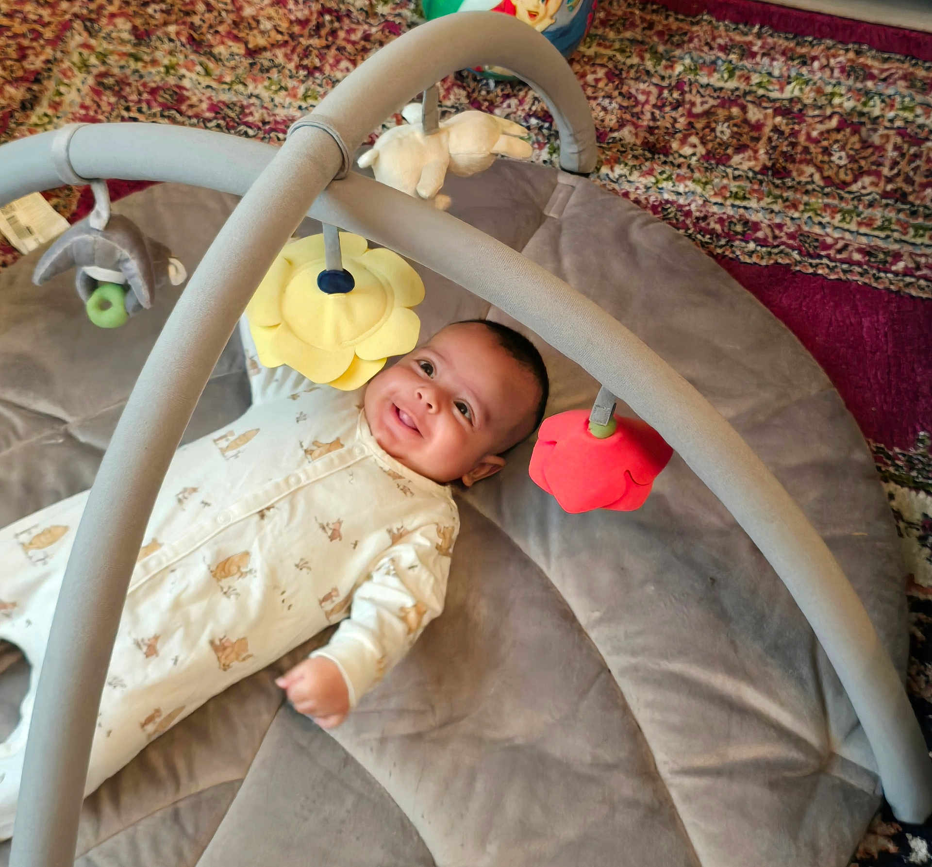 Jibran is registered to the contest to win money with this photo: baby, infant, play_mat, toy, smile, happy, lying_down, soft_toys, colorful, indoor, child, cute, onesie, patterned_rug, plush, face, portrait, baby_toys, baby_gym, cozy