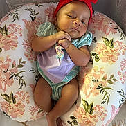 Calliope is registered to the contest to win money with this photo: baby, infant, headband, red_bow, floral_cushion, pastel_colors, hands_clasped, cute, comfortable, soft_lighting, lying_down, baby_clothing, patterned_cushion, indoor, portrait, young_child, resting, peaceful, skin, expression