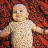 Willow-Ann is registered to the contest to win money with this photo: baby, infant, child, smiling, portrait, lying_down, floral_clothing, red_blanket, patterned_blanket, indoors, face, eyes, arms, outstretched_arms, clothing, textile, happy, cute, close_up, photography