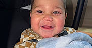 Leonidas is registered to the contest to win money with this photo: baby, child, car_seat, blanket, smile, happy, face, rosy_cheeks, clothing, checkered_shirt, indoor, person, portrait, cute, hands, young_child, infant, seat_belt, car, soft_texture