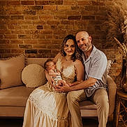 Enzo joined the competition — help win amazing prizes! family, baby, newborn, mother, father, couch, brick_wall, indoor, portrait, smile, dress, beige, wooden_floor, pampas_grass, decor, intimate, warm_lighting, seated, happy, people