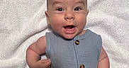Enzo is registered to the contest to win money with this photo: baby, infant, smiling, blue_onesie, button_clothing, towel, white_background, happy, portrait, cute, child, skin, head, eyes, mouth, arms, hand, sitting, expression, indoor