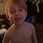 Azlan is registered to the contest to win money with this photo: child, toddler, smiling, indoor, shirtless, living_room, television, cartoon, furniture, tile_floor, blond_hair, happy, person, home, casual, standing, playful, young_child, cute, boy