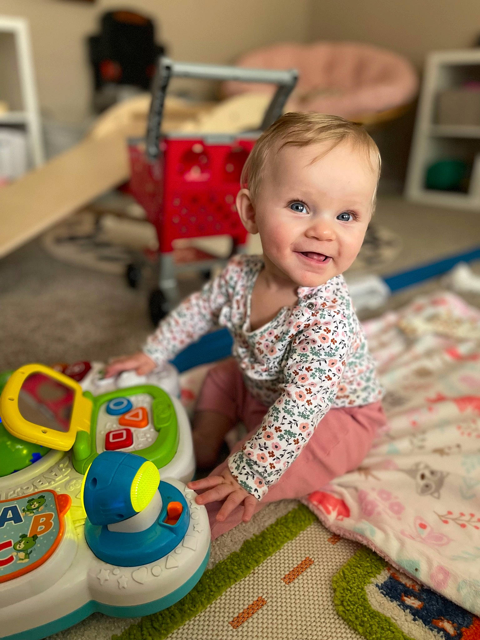 Kamryn is registered to the contest to win money with this photo: baby, baby_products, baby_toddler_clothing, child, event, facial_expression, flooring, fun, happy, joy, leisure, person, plastic, play, product, room, sitting, smile, toddler, toy