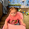 child, toddler, high_chair, pink, pigtails, shirt, text, toy, floor, box, bluey, cartoon, wooden_floor, indoor, furniture, person, cute, playful, scattered_toys, casual