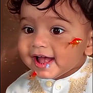 Enzo is registered to the contest to win money with this photo: toddler, child, face, curly_hair, big_eyes, smile, white_clothing, embroidered_outfit, goldfish, fish, cute, portrait, indoor, happy, closeup, baby, person, expression, funny, colorful