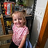 child, toddler, smiling, pigtails, indoor, kitchen, snacks, pantry, shelf, light_switch, wooden_doorframe, clothing, pink_shirt, black_pants, person, happy, standing, handrail, face, hair