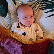 Gabin participe au concours pour gagner de l'argent avec cette photo : baby, infant, smile, blanket, knitted, bedspread, leaf_pattern, clothing, cozy, lying_down, cute, face, expression, indoors, comfort, small_child, happy, young, person, portrait