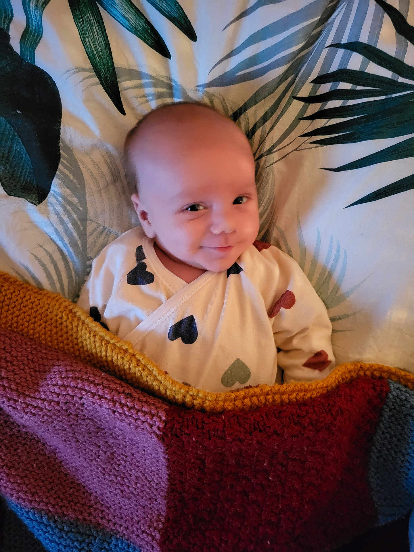 Gabin participe au concours pour gagner de l'argent avec cette photo : baby, infant, smile, blanket, knitted, bedspread, leaf_pattern, clothing, cozy, lying_down, cute, face, expression, indoors, comfort, small_child, happy, young, person, portrait