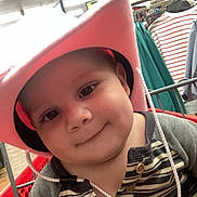 Kyle is registered to the contest to win money with this photo: baby, cart, child, close_up, clothing_rack, clothing_store, cowboy_hat, face, fluorescent_lighting, gray_clothing, happy, indoor, pink_hat, portrait, retail, shopping, shopping_cart, smiling, store, striped_shirt