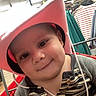 baby, cart, child, close_up, clothing_rack, clothing_store, cowboy_hat, face, fluorescent_lighting, gray_clothing, happy, indoor, pink_hat, portrait, retail, shopping, shopping_cart, smiling, store, striped_shirt