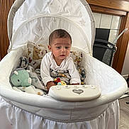 Liam joined the competition — help win amazing prizes! baby, infant, child, sitting, bassinet, crib, blanket, plush_toy, dinosaur_toy, stuffed_animal, baby_clothing, white_clothing, face, portrait, indoors, nursery, furniture, wood_paneling, curious, safe