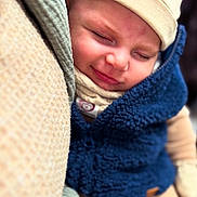 Elias is registered to the contest to win money with this photo: baby, child, sleeping, smiling, face, hat, clothing, warm, cozy, blue_vest, beige, blanket, soft, portrait, cute, infant, closeup, peaceful, resting, nap