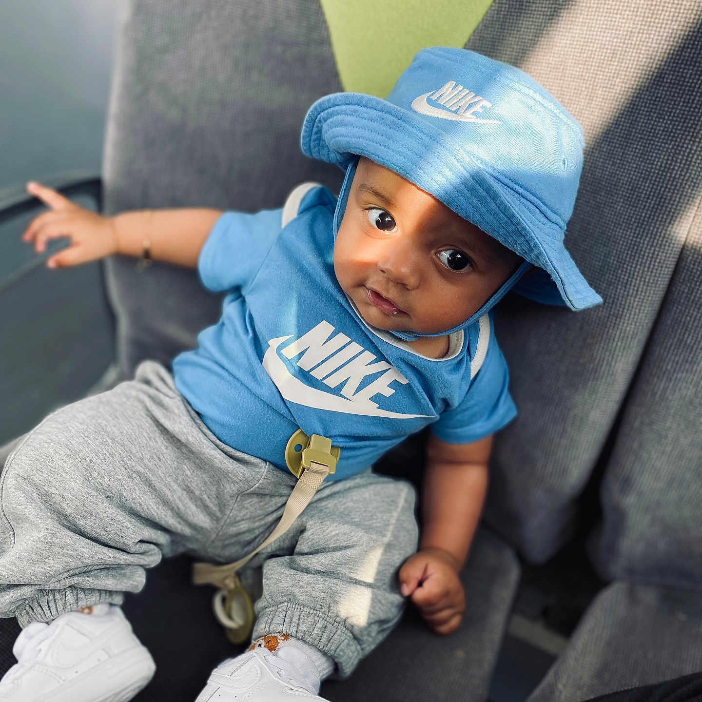 Alisson Nzambi participe au concours pour gagner de l'argent avec cette photo : baby, blue_clothing, bucket_hat, casual, chair, child, comfortable, curious_expression, cute, fashion, gray_pants, indoor, infant, nike_logo, person, portrait, shadow, sitting, sunlight, white_shoes