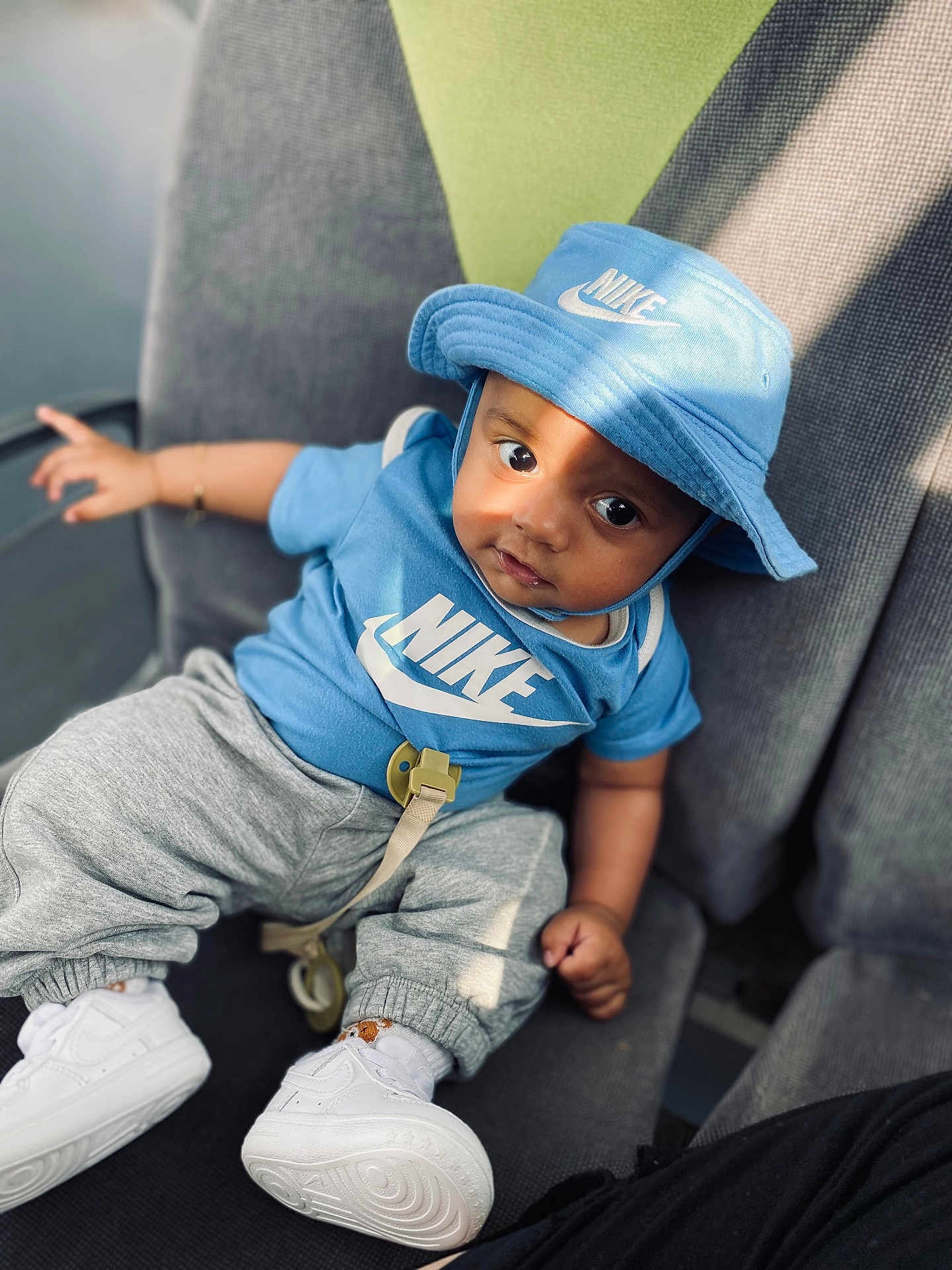 Alisson Nzambi participe au concours pour gagner de l'argent avec cette photo : baby, blue_clothing, bucket_hat, casual, chair, child, comfortable, curious_expression, cute, fashion, gray_pants, indoor, infant, nike_logo, person, portrait, shadow, sitting, sunlight, white_shoes