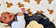Alisson Nzambi participe au concours pour gagner de l'argent avec cette photo : baby, blanket, child, clothing, cloud_shape, cute, denim_overalls, face, hand, indoors, infant, lying_down, milestone, newborn, portrait, smiling, soft_texture, teddy_bear_pattern, white_shirt, wooden_sign