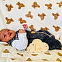 baby, blanket, child, clothing, cloud_shape, cute, denim_overalls, face, hand, indoors, infant, lying_down, milestone, newborn, portrait, smiling, soft_texture, teddy_bear_pattern, white_shirt, wooden_sign