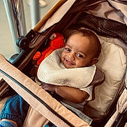 Alisson Nzambi participe au concours pour gagner de l'argent avec cette photo : baby, baby_boy, bib, blue_pants, child, clothing, cozy, cute, footwear, happy, indoor, infant, orange_toy, person, portrait, seat, smile, socks, stroller, toy