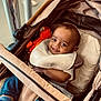 baby, baby_boy, bib, blue_pants, child, clothing, cozy, cute, footwear, happy, indoor, infant, orange_toy, person, portrait, seat, smile, socks, stroller, toy