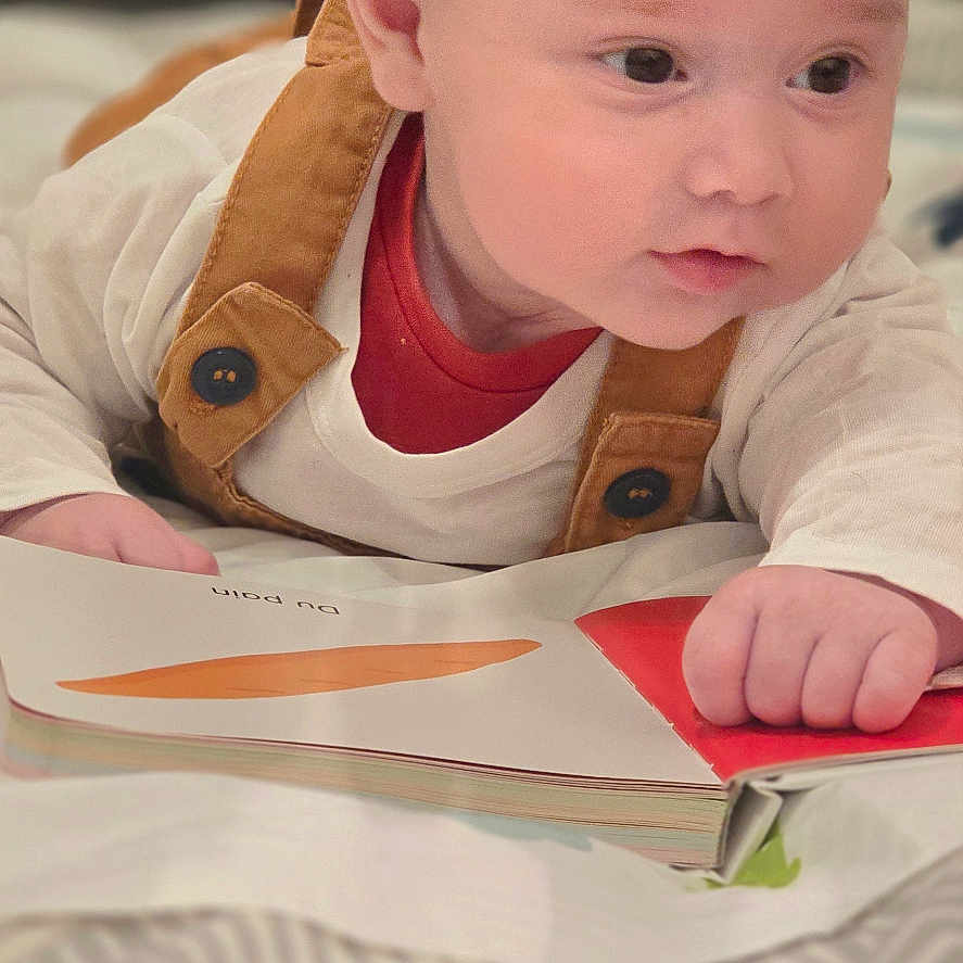 Brayan-Adam a rejoint le concours — aidez-le/la à gagner de superbes lots ! baby, bedroom, blanket, book, brown, child, closeup, cozy, curious, face, hand, indoor, infant, overalls, portrait, reading, soft_lighting, toddler, white_shirt, young_child