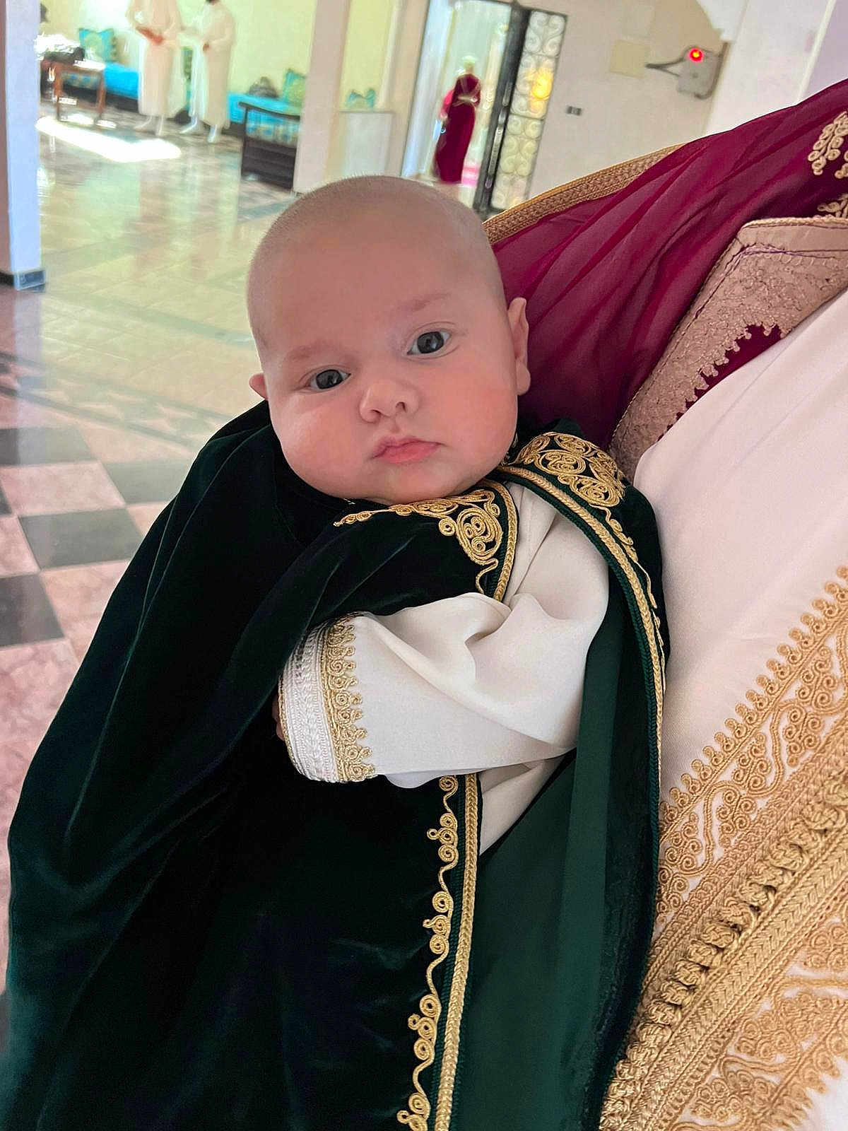Brayan-Adam a rejoint le concours — aidez-le/la à gagner de superbes lots ! baby, child, person, traditional_clothing, embroidery, portrait, indoor, holding, face, curious, chubby_cheeks, head, black_clothing, gold_detail, people, background, floor, light, wall, door