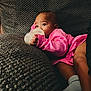 baby, bottle, pink_clothing, couch, texture, infant, milk, hand, face, eyes, socks, relaxing, indoor, person, comfort, child, young, resting, soft, casual