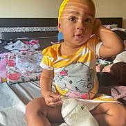 Samari is registered to the contest to win money with this photo: toddler, child, baby_bottle, bed, blanket, yellow_headband, elephant_dress, milk, indoor, person, cute, smile, sitting, sunlight, striped_light, soft_toys, pink, cozy, casual, portrait
