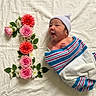 newborn, baby, infant, portrait, lying_down, swaddled, blanket, hat, flowers, roses, dahlias, greenery, pink, colorful, indoor, white_background, floral_arrangement, peaceful, cute, photography