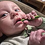 baby, infant, close_up, face, hand, green_bean, eating, teething, mouth, eyes, onesie, clothing, indoor, couch, blanket, finger, curiosity, feeding, newborn, portrait