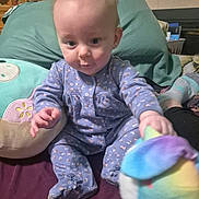 Lexi is registered to the contest to win money with this photo: baby, infant, child, onesie, pajamas, plush_toy, stuffed_animal, pillow, blanket, bed, sitting, face, eyes, hands, feet, smile, home_interior, furniture, patterned_clothing, portrait