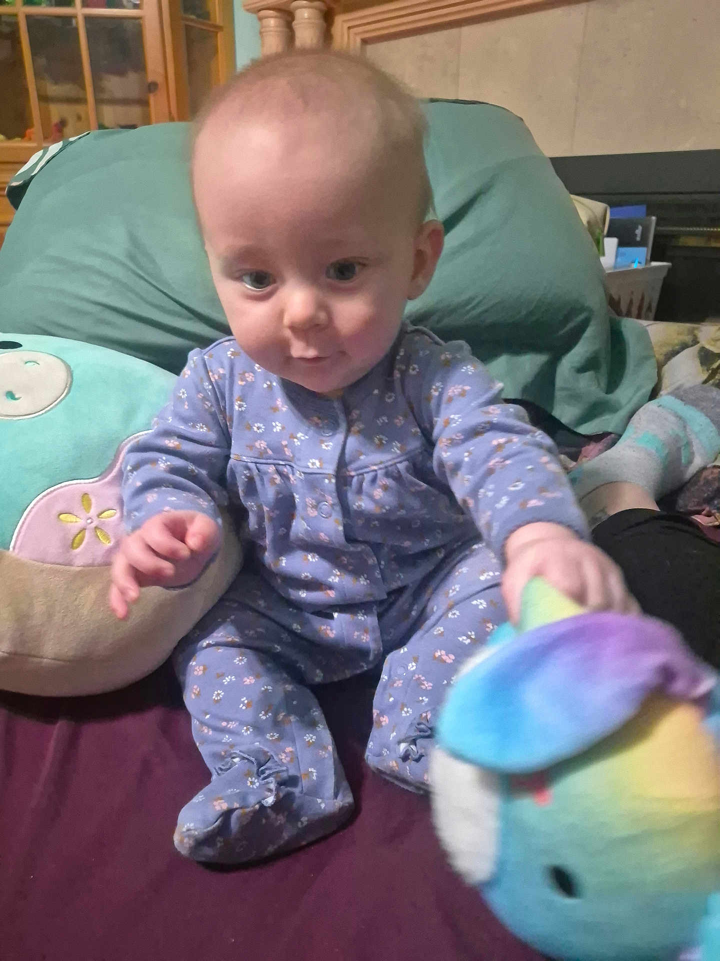 Lexi is registered to the contest to win money with this photo: baby, infant, child, onesie, pajamas, plush_toy, stuffed_animal, pillow, blanket, bed, sitting, face, eyes, hands, feet, smile, home_interior, furniture, patterned_clothing, portrait