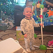 Cameron joined the competition — help win amazing prizes! toddler, child, pajamas, sheep_pattern, baby_toys, activity_center, christmas_tree, living_room, carpet, sofa, holiday_decor, smiling, indoors, toy_box, baby, person, playtime, festive, home, cute