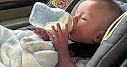 Grayson is registered to the contest to win money with this photo: baby, blanket, bottle, car_interior, car_seat, child, child_seat, comfort, cozy, cute, daylight, feeding, infant, milk, person, relaxing, seat, transportation, window, young_child