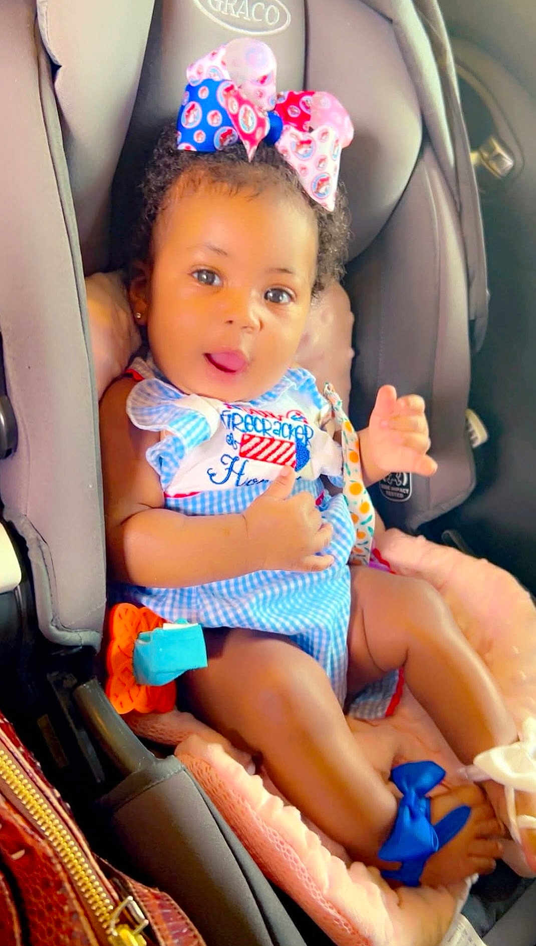 Honesty joined the competition — help win amazing prizes! baby, child, car_seat, bow, dress, blue, pink, cushion, infant, cute, tongue_out, clothing, footwear, ribbon, seatbelt, indoor, person, happy, portrait, car_interior