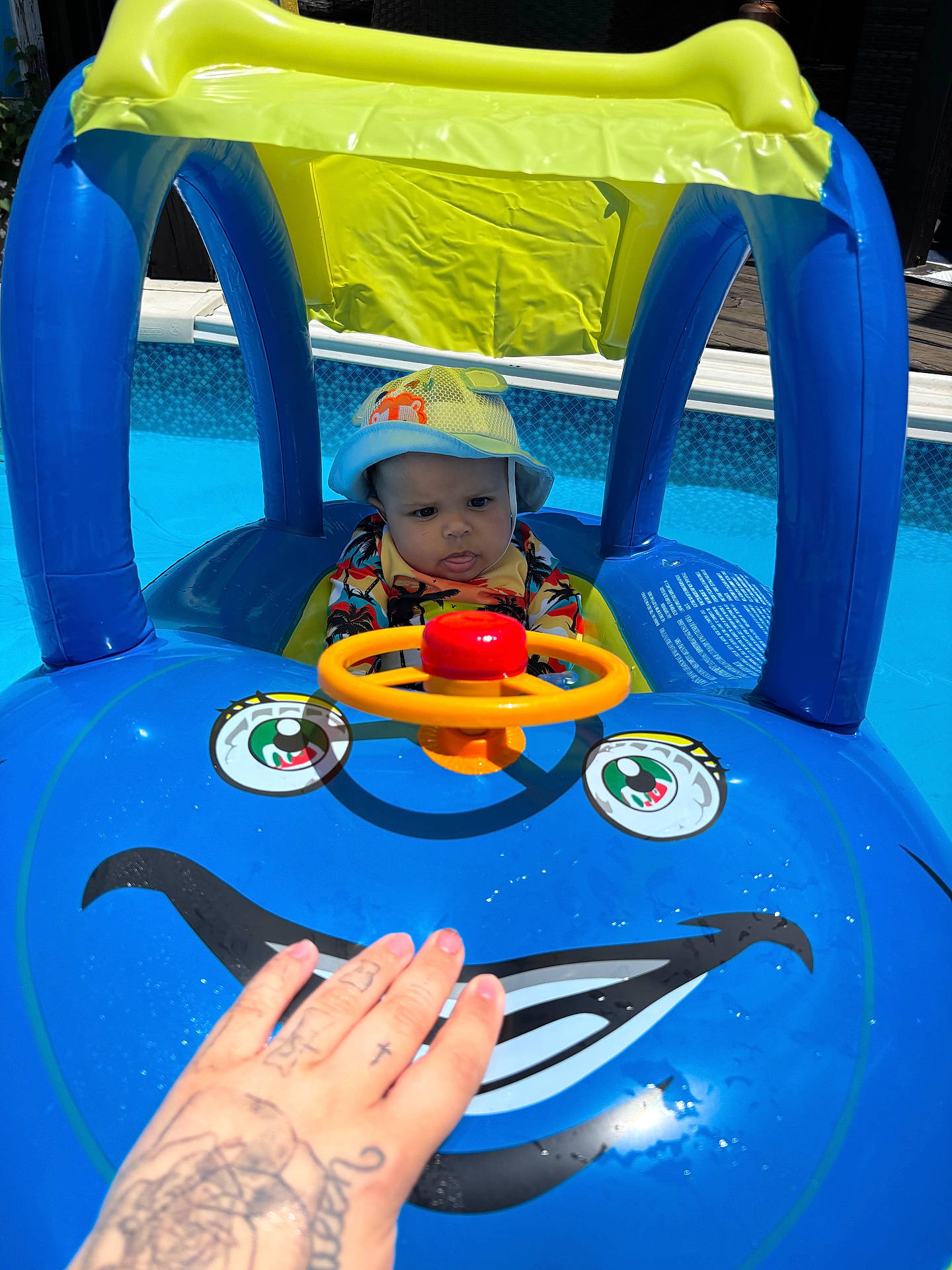 baby, blue, child, expression, face, float, fun, hand, inflatable, outdoor, play, pool, summer, sunhat, sunny, swimwear, tattoo, toy, water, yellow