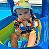 baby, child, pool, inflatable, swimsuit, hat, sunhat, water, blue, summer, outdoor, playful, tongue_out, sitting, cute, colorful, sunny, vacation, toddler, fun
