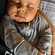 Kamari is registered to the contest to win money with this photo: baby, sleeping, infant, hands, clothing, dinosaur_pattern, rainbow_pattern, closeup, portrait, peaceful, cozy, soft_light, human, child, cute, resting, person, fabric, texture, indoor