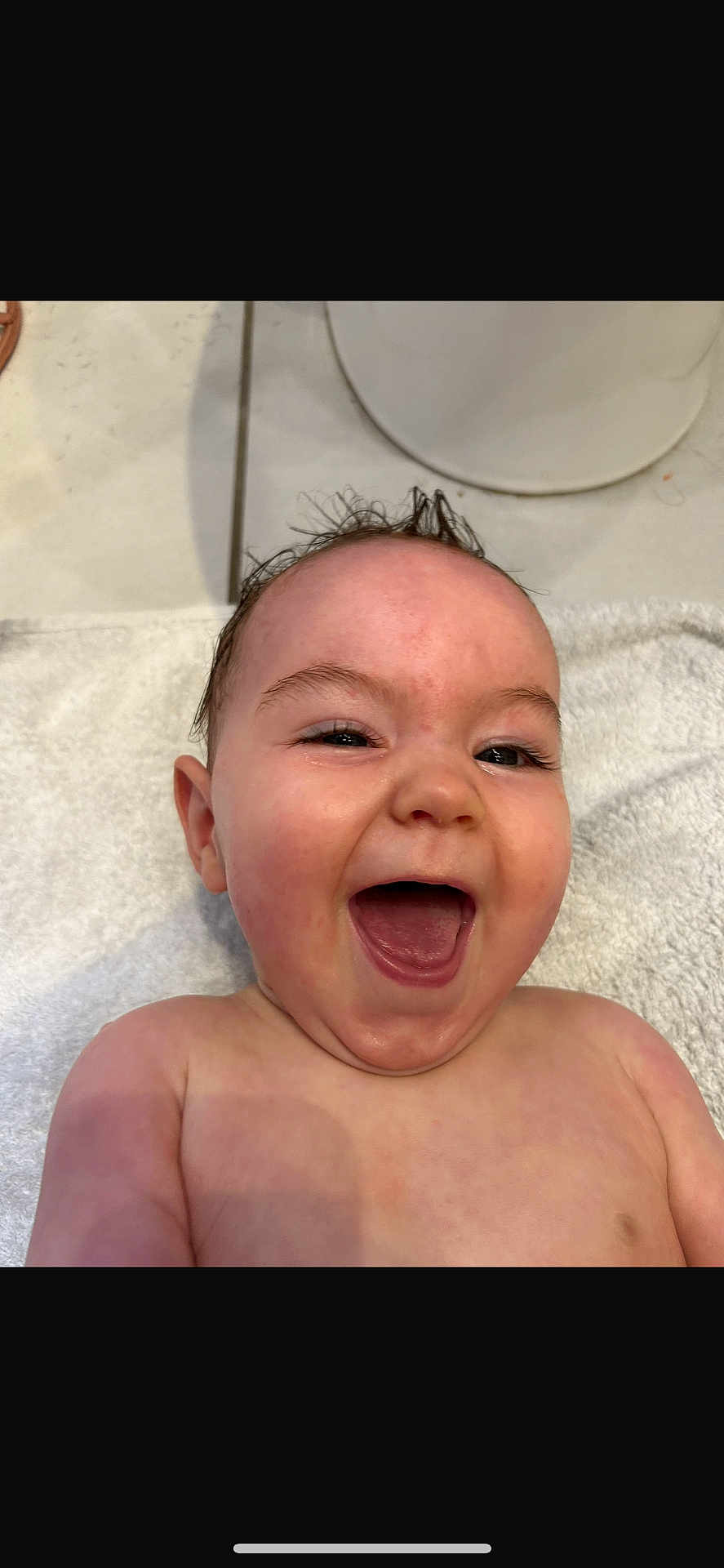 Skye is registered to the contest to win money with this photo: baby, infant, laughing, happy, wet_hair, mohawk, towel, skin, face, mouth_open, teeth, floor, tile, ear, shoulder, child, indoors, expression, joy, mouth