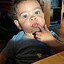 Jac is registered to the contest to win money with this photo: toddler, child, blue_eyes, curly_hair, finger_in_mouth, indoor, table, shirt, person, face, cute, expression, skin, light, shadow, young_child, curiosity, portrait, seated, casual