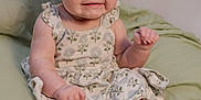 Skylar is registered to the contest to win money with this photo: baby, child, smile, dress, floral, green_blanket, sitting, cute, indoors, infant, happy, cheeks, barefoot, portrait, young_child, playful, clothing, person, skin, expression
